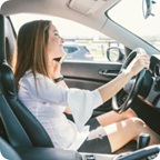 Woman smiles as she drives and talks on a cell phone. 